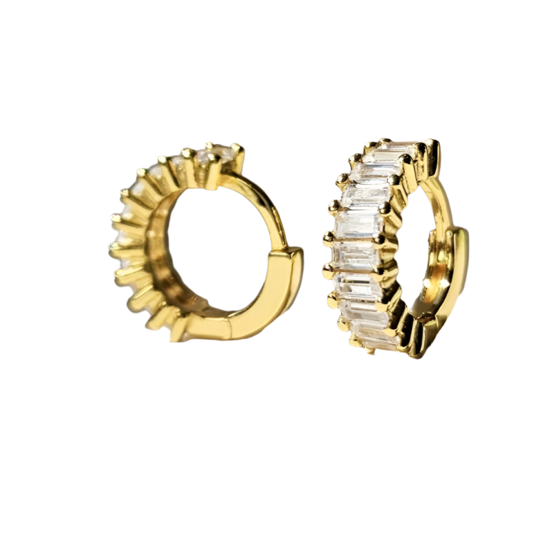 A pair of gold-plated sterling silver huggie hoop earrings. The front of the huggies are encrusted with a column of horizontal baguette shaped white cubic zirconia.  The earrings are floating against a white background. One earring is facing forward and the other is facing to the side showing the inside of the hoop.