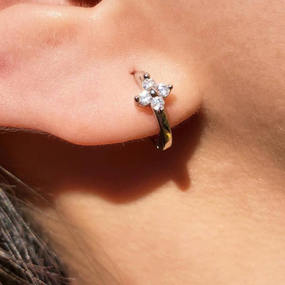 Close-up of a model wearing a small gold-plate sterling silver huggie hoop earring. The earring has a small flower detail. The flower is made of 4 white cubic zirconia with surrounding a gold center.
