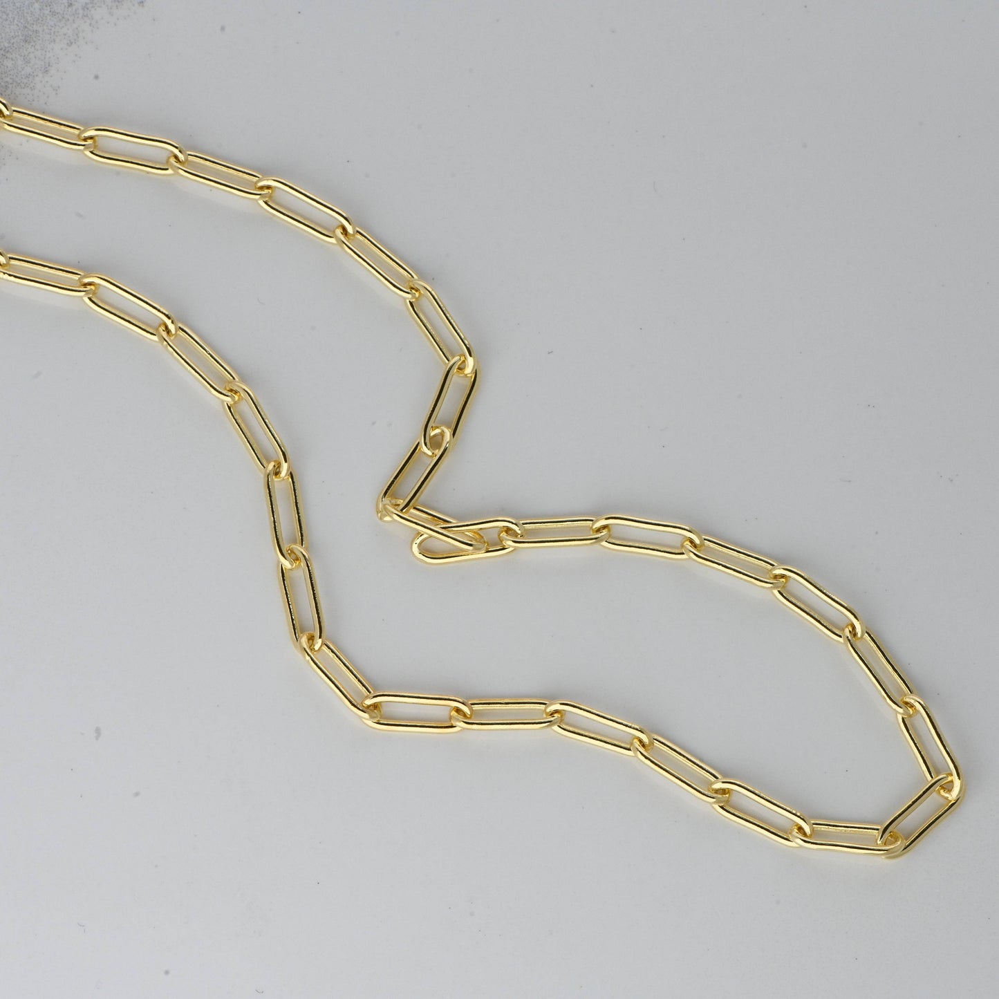 A gold-plated sterling silver paperclip style necklace. The links in the necklace are oval resembling a paperclip. The necklace is laying on a smooth white stone surface.