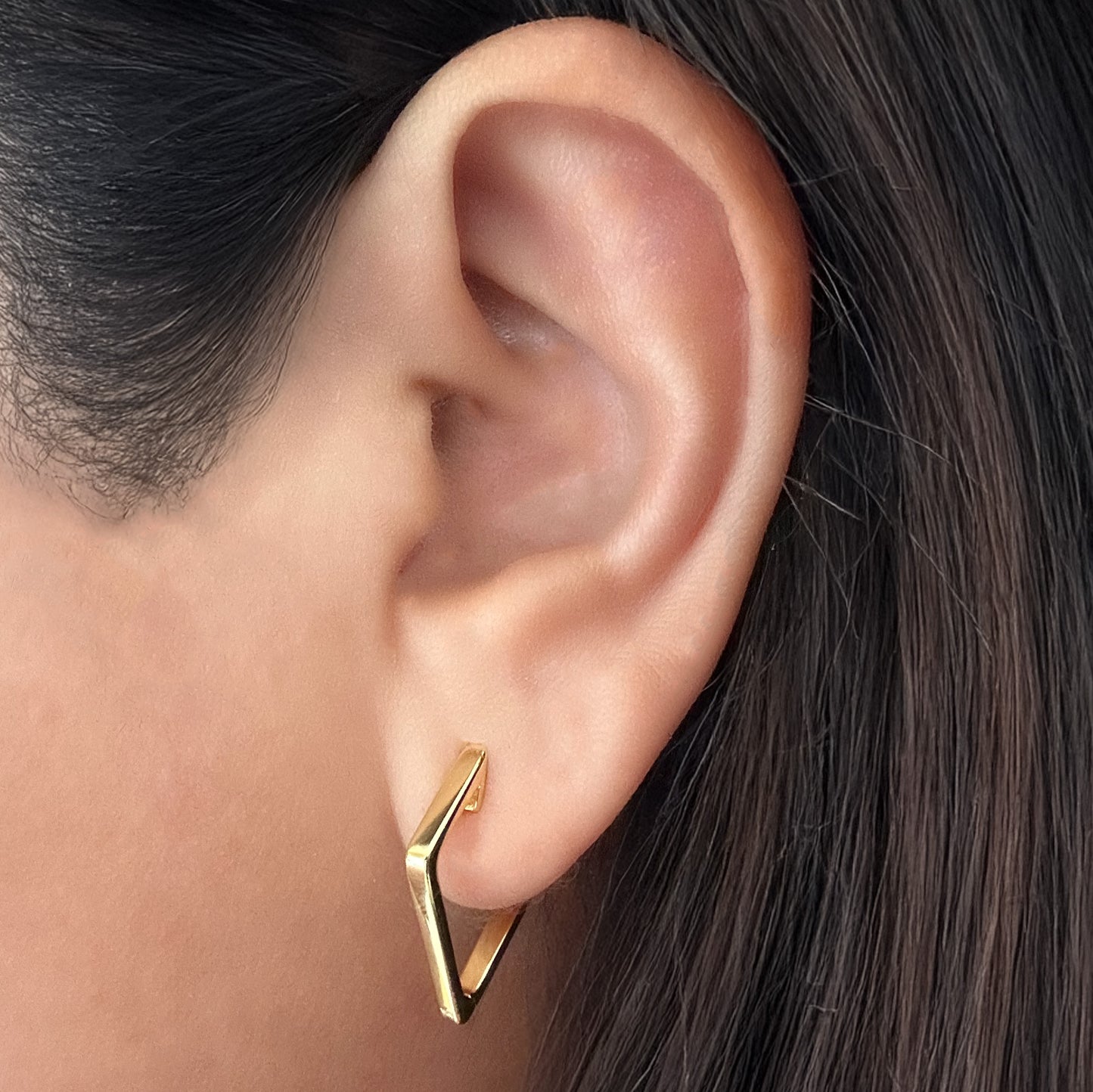 Model wearing a gold-plated sterling silver kite-shaped hoop earring. The model's ear is facing slightly to the left to show the shape of the hoop.
