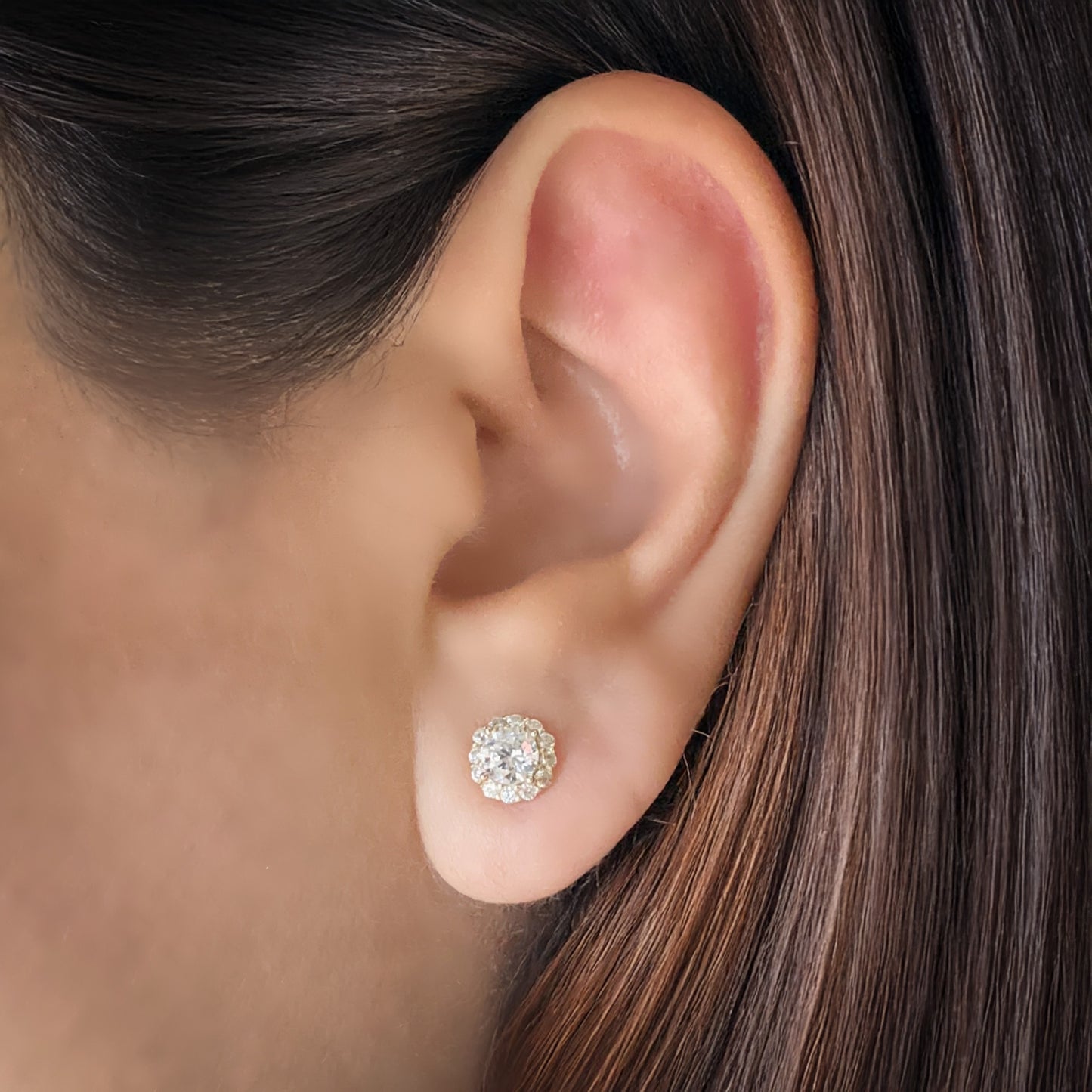 Model wearing a gold-plated sterling silver white cubic zirconia stud earring. The earring has 12 small stones surround a larger round stone in the center.