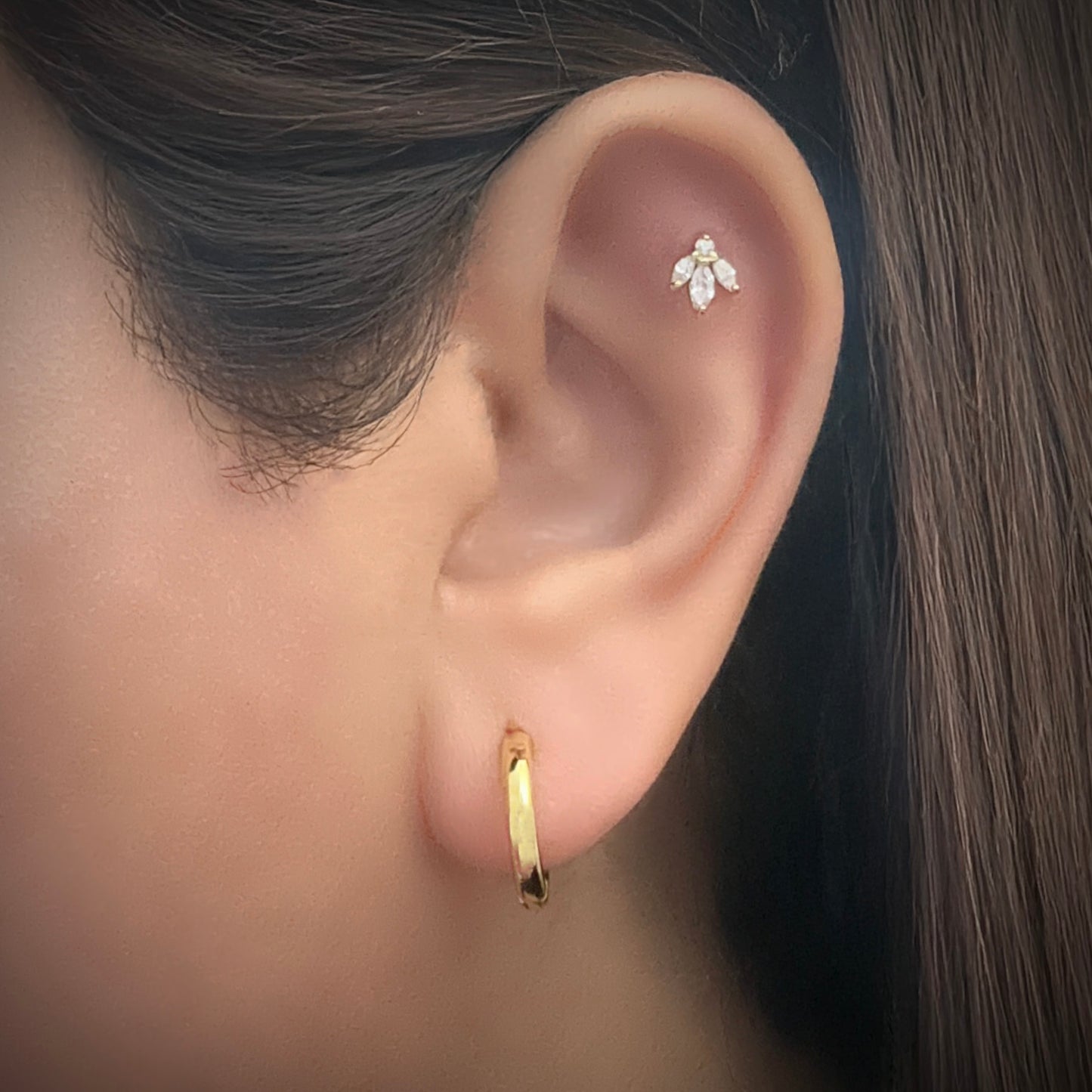 Model is wearing a slightly chunky gold-plated sterling silver hoop. She is also wearing a gold-plated sterling silver flower-shaped stud earring in the flat part of her ear just under the upper helix. The flower stud has 3 petals made from marquis-cut white cubic zirconia attached to a round-cut white cubic zirconia.
