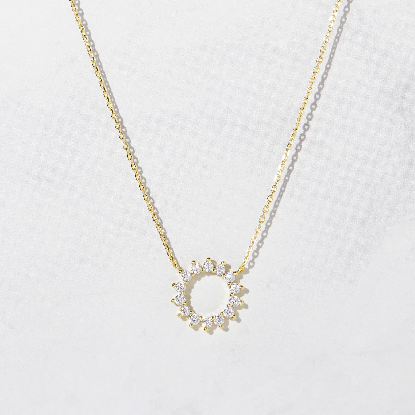 Delicate gold-plated sterling silver necklace with a circular pendant. The pendant is an open circle with 12 white cubic zirconia stones set around the circumference.