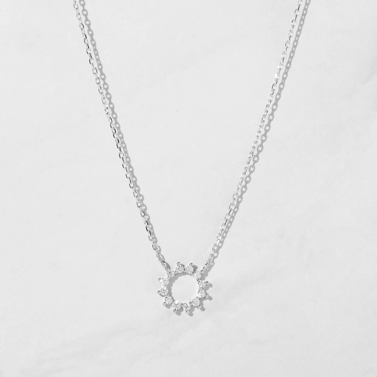 Delicate sterling silver necklace with a circular pendant. The pendant is an open circle with 12 white cubic zirconia stones set around the circumference.