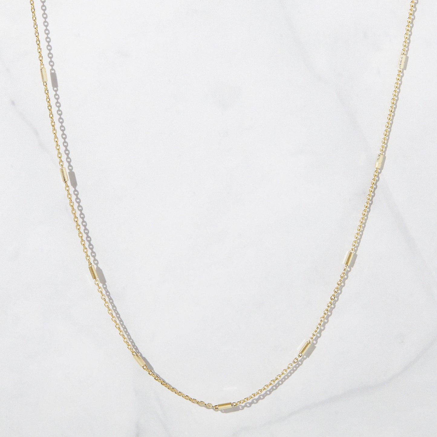 Gold-plated sterling silver delicate chain necklace with elongated gold bead-like elements approximately every two inches. The chain is dangling against a white backdrop.