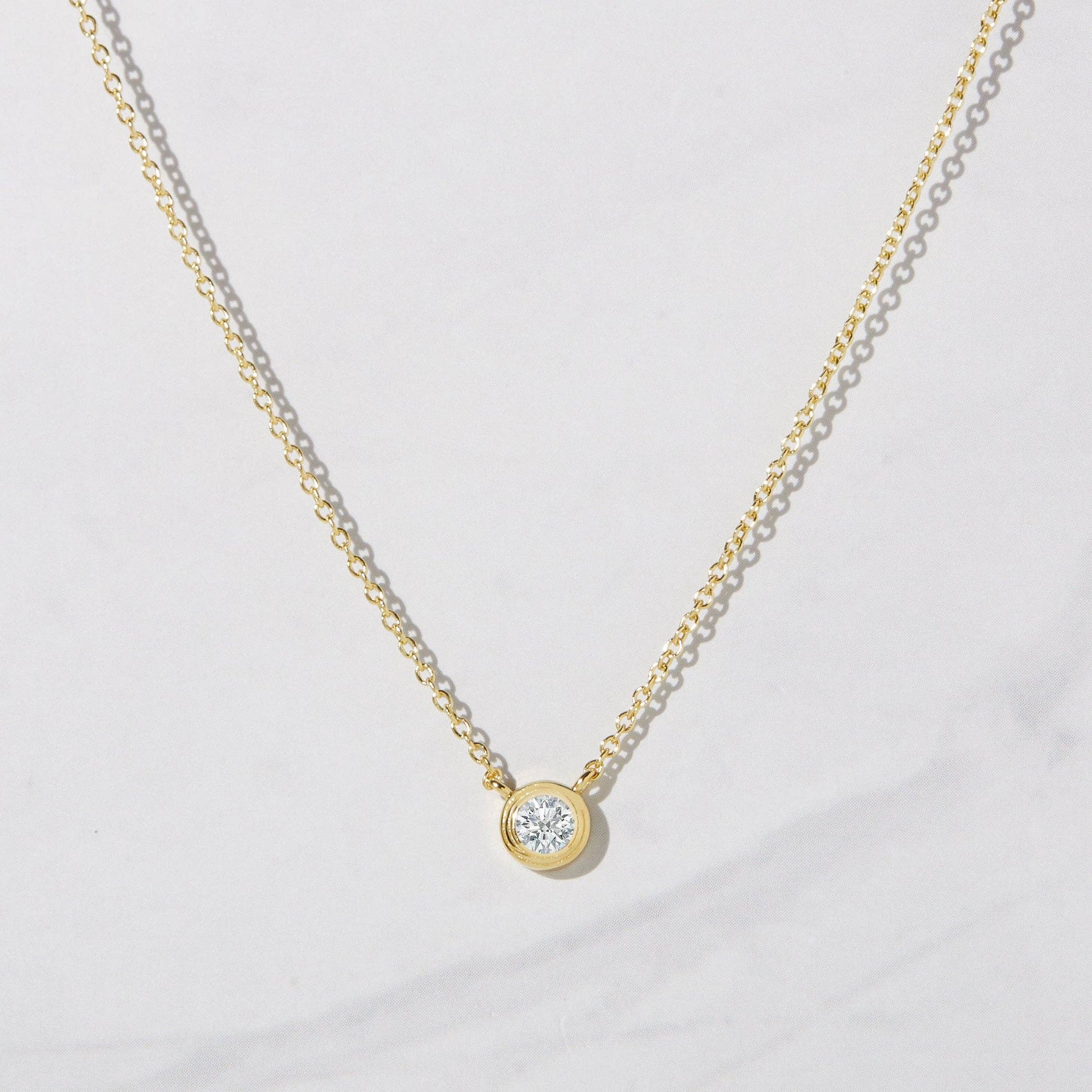 Gold-plated delicate chain necklace with bezel set white cubic zirconia pendant connected to the chain. 