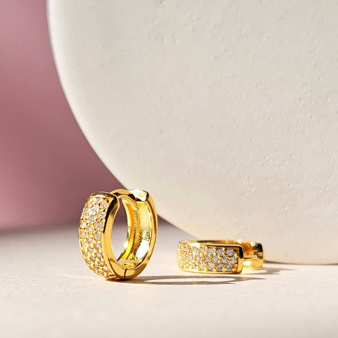 A pair of gold-plated sterling silver huggie hoop earrings. The earrings have 3 columns of white cubic zirconia set in a pave style. One earring is on its side while the other is standing up showing the detail of the hoop.