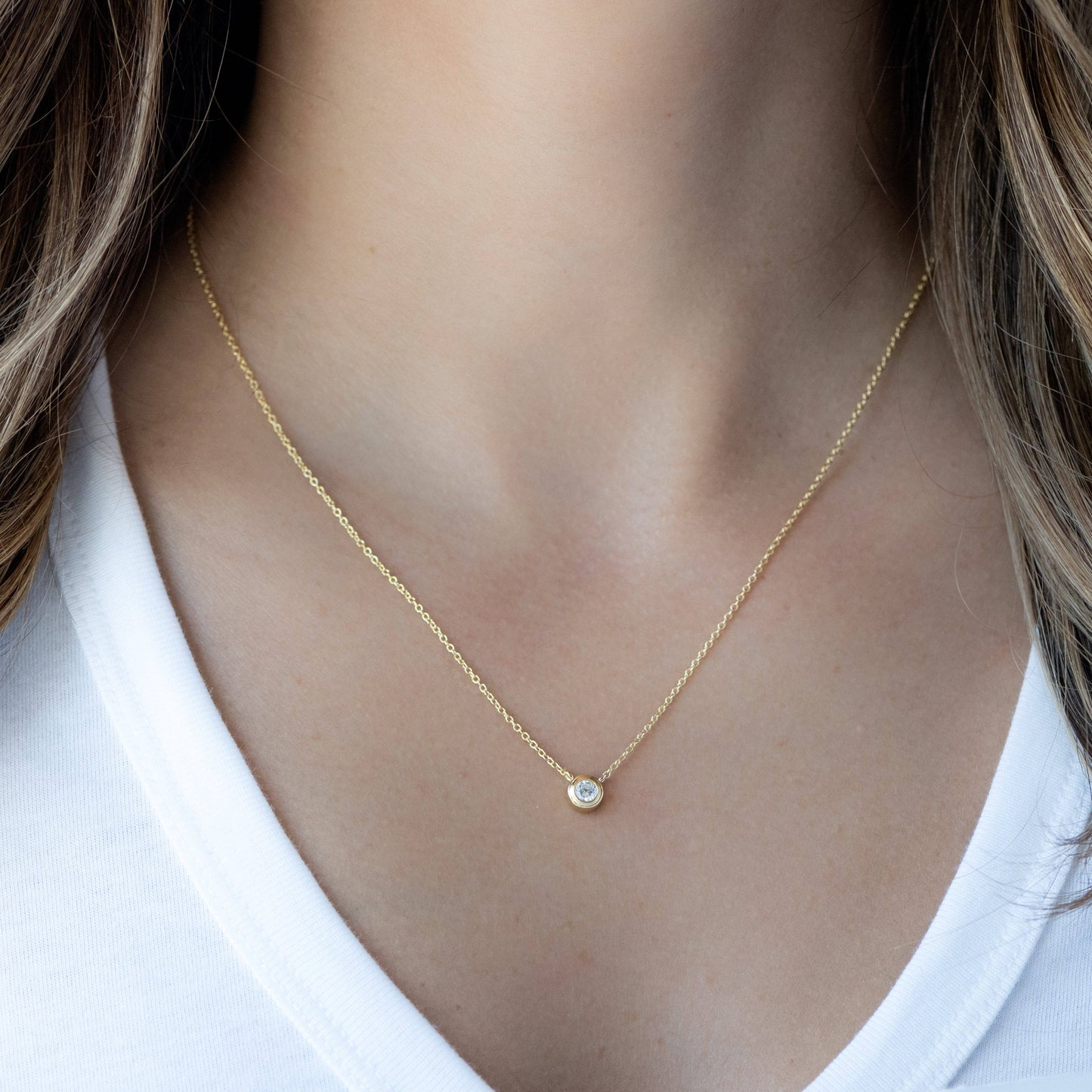 Model wearing a gold-plated delicate chain necklace with bezel set white cubic zirconia pendant connected to the chain.