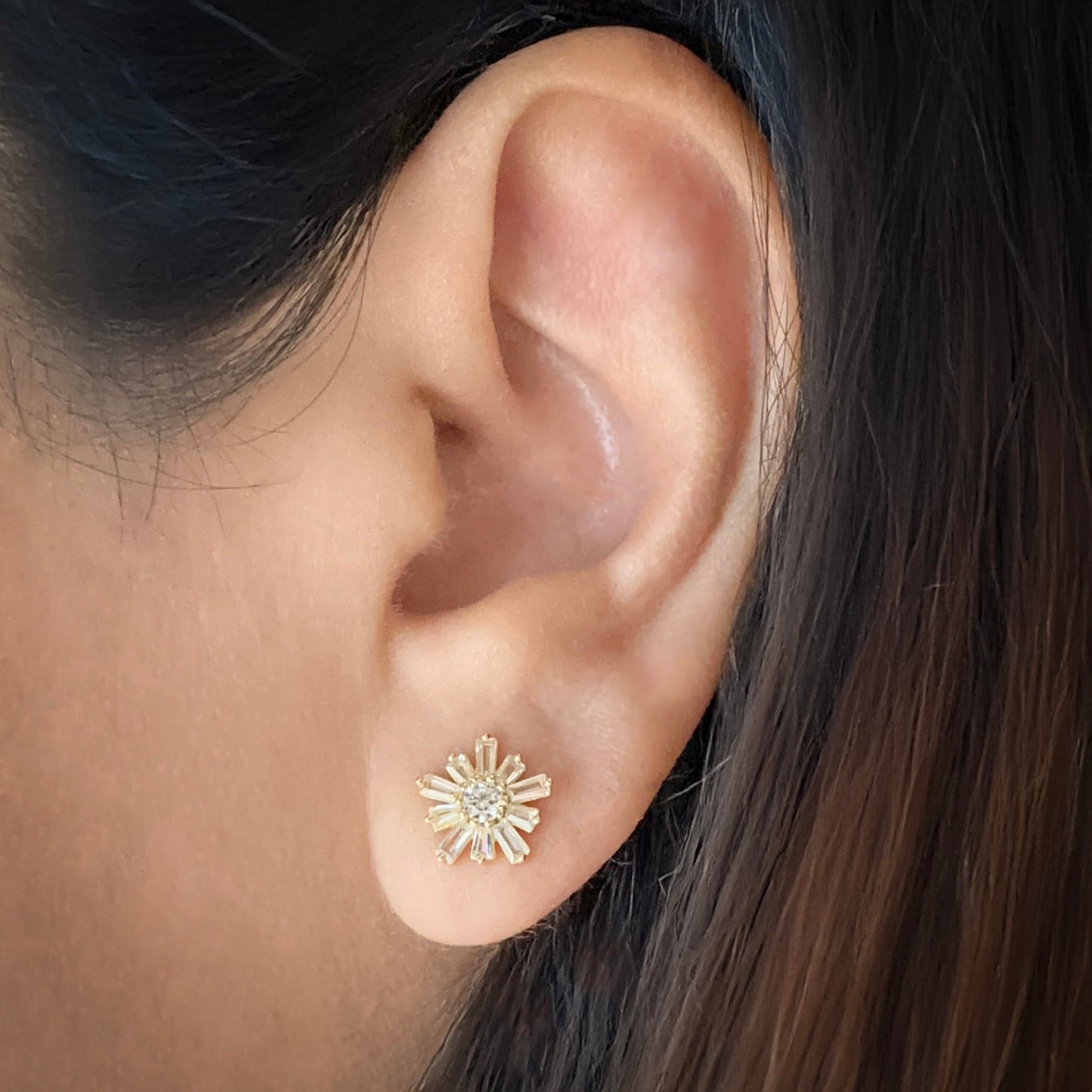 Model wearing Sterling silver flower-shaped studs earrings with 10 petals and a circular stone in the center. The image focuses on one ear with the earring in a traditional lobe piercing. Each petal is made of white cubic zirconia in a baguette shape. The center stone is white cubic zirconia. 