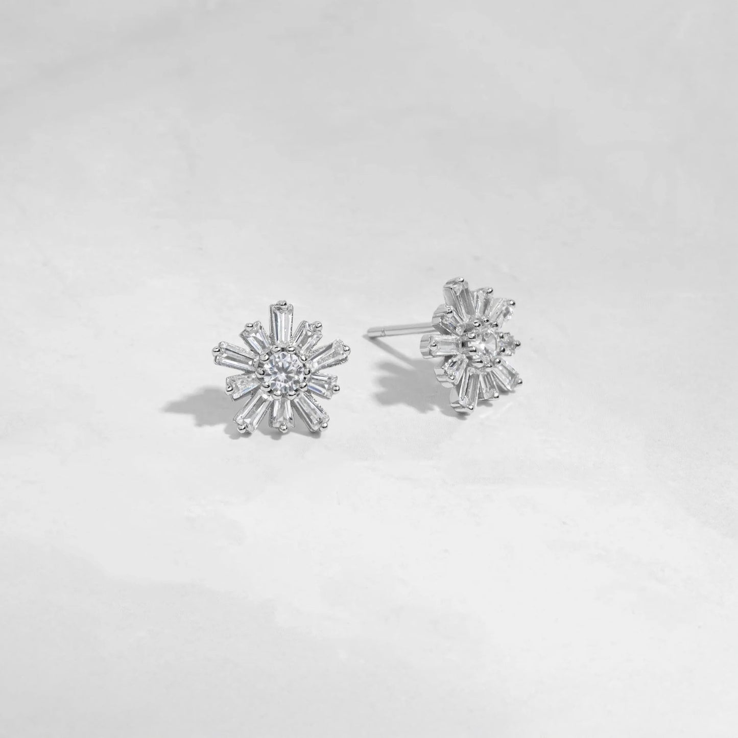 Sterling silver flower-shaped studs earrings with 10 petals and a circular stone in the center. Each petal is made of white cubic zirconia in a baguette shape. The center stone is white cubic zirconia. 