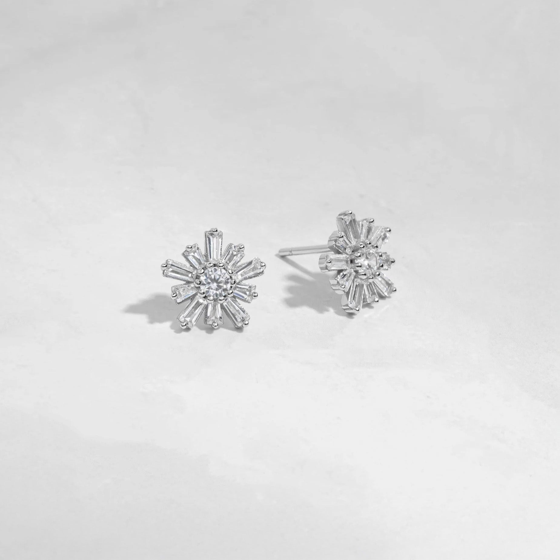 Sterling silver flower-shaped studs earrings with 10 petals and a circular stone in the center. Each petal is made of white cubic zirconia in a baguette shape. The center stone is white cubic zirconia. 