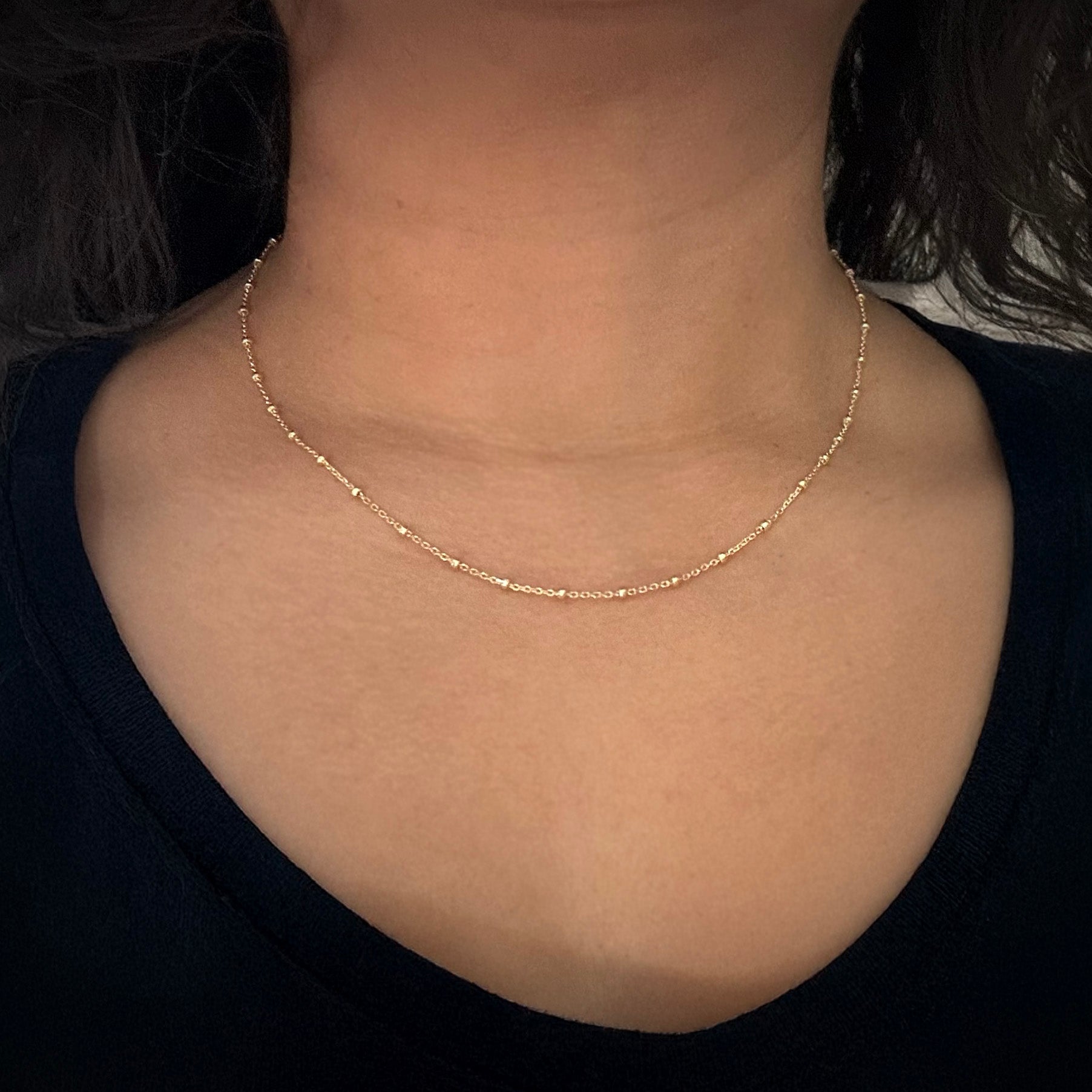 Model wearing a dainty gold-plated sterling silver chain with gold beads. The beads are separated by one inch of chain. 