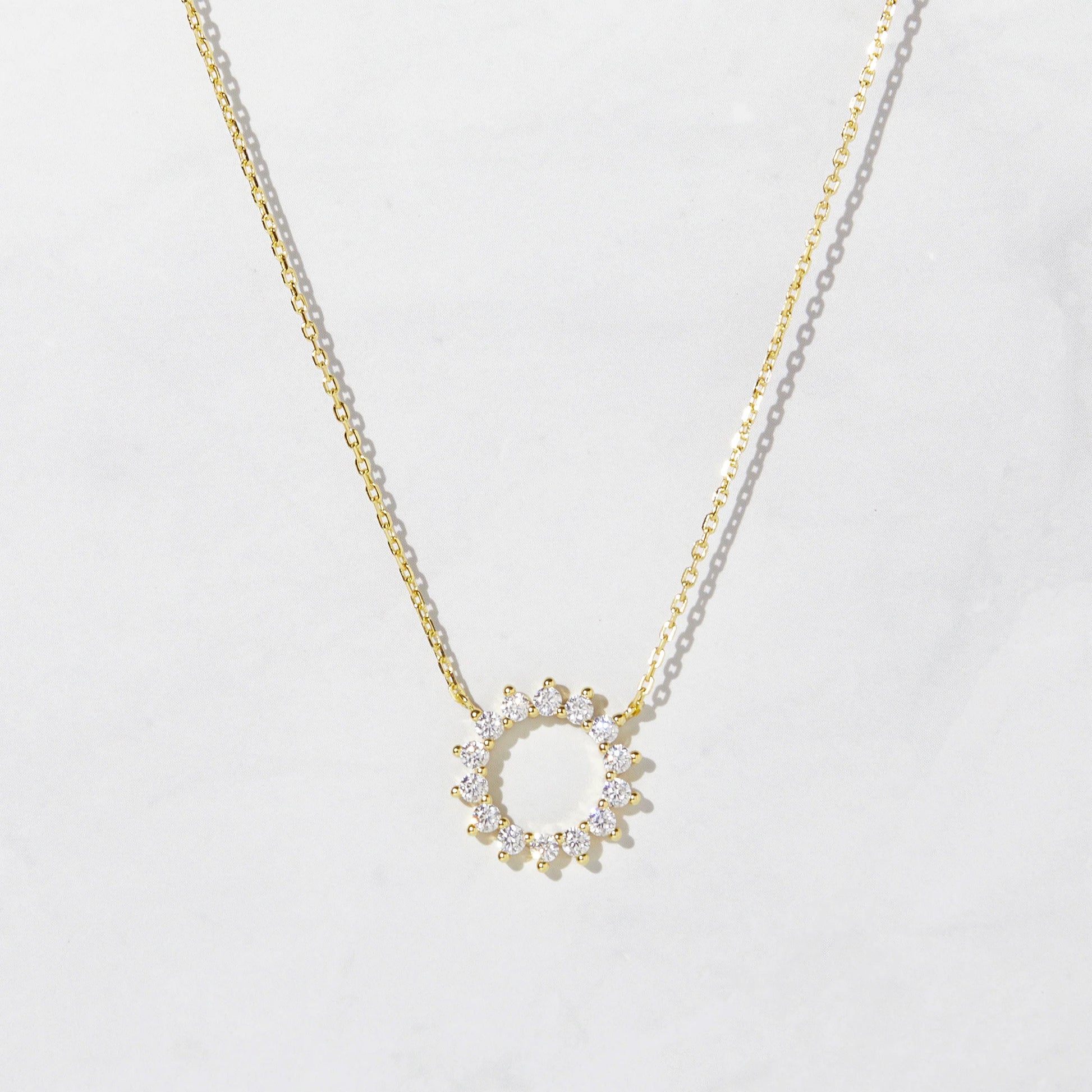Delicate gold-plated sterling silver necklace with a circular pendant. The pendant is an open circle with 12 white cubic zirconia stones set around the circumference. 