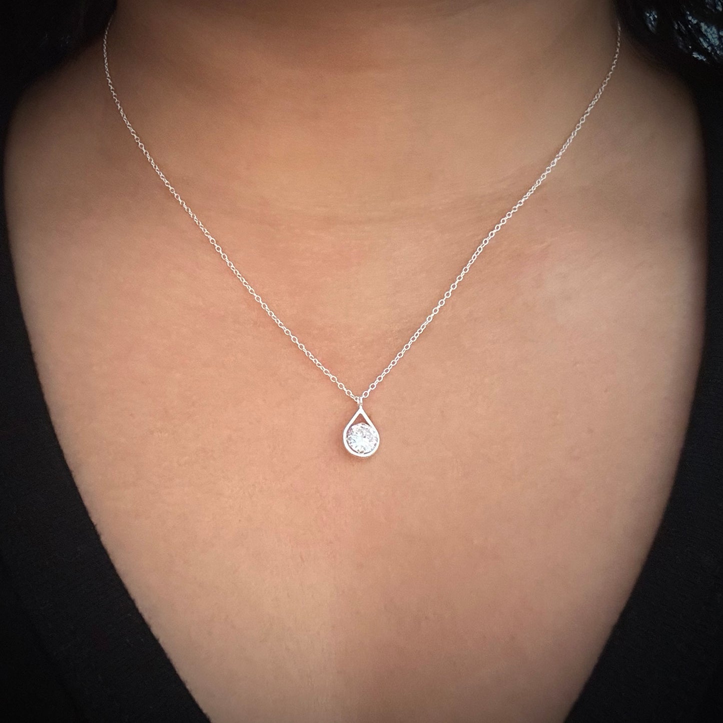 Model wearing a sterling silver chain necklace with a tear drop shaped pendant. In the pendant is a round white cubic zirconia. 