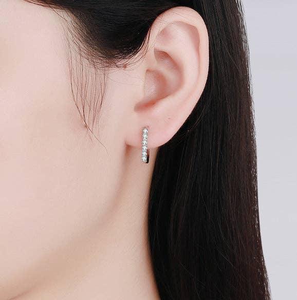 A model wearing a platinum-plated sterling silver oval hinged hoop with 6 round-cut moissanite stones. 