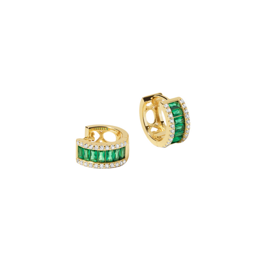 A pair of small gold-plated sterling silver huggie hoops floating against a white backdrop. Each hugggie is set with a column of horizontal baguette cut green cubic zirconia. On either side of this column are small white cubic zirconia. One huggie is facing slightly to the right showing a circular gold detail on the back of the earring. The other earring is sitting on its side.